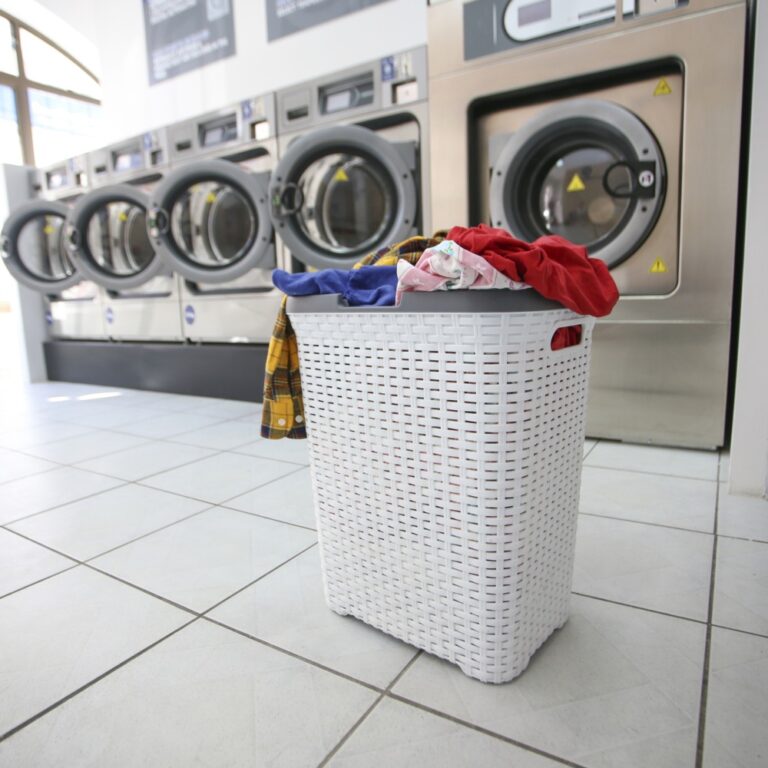 Laundry basket full of dirty clothes and washing machines in a laundromat.